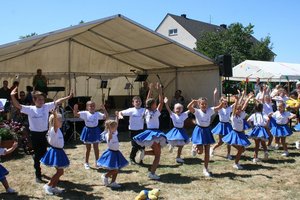Mädchen tanzen in blauen Karnevalskostümen auf der Wiese vor einem Festzelt