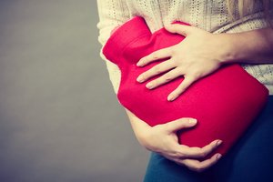 Eine Frau hält einen Wärmflasche vor den Bauch