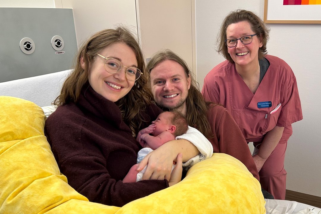 Das Bild zeigt die frischgebackenen Eltern Judith Rossow und Christopher Kintrup mit Zoe sowie Stationshebamme Manuela Breuer.