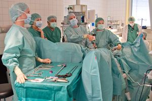 In einem Operationssaal stehen mehrere Ärzte an einem Operationstisch und beobachten einen Monitor.