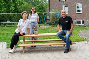 Drei Personen stehen und sitzen um einen Gartentisch herum