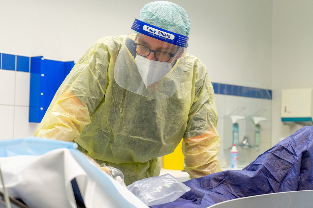 Ein Arzt in Schutzkleidung beugt sich über eine Patientin