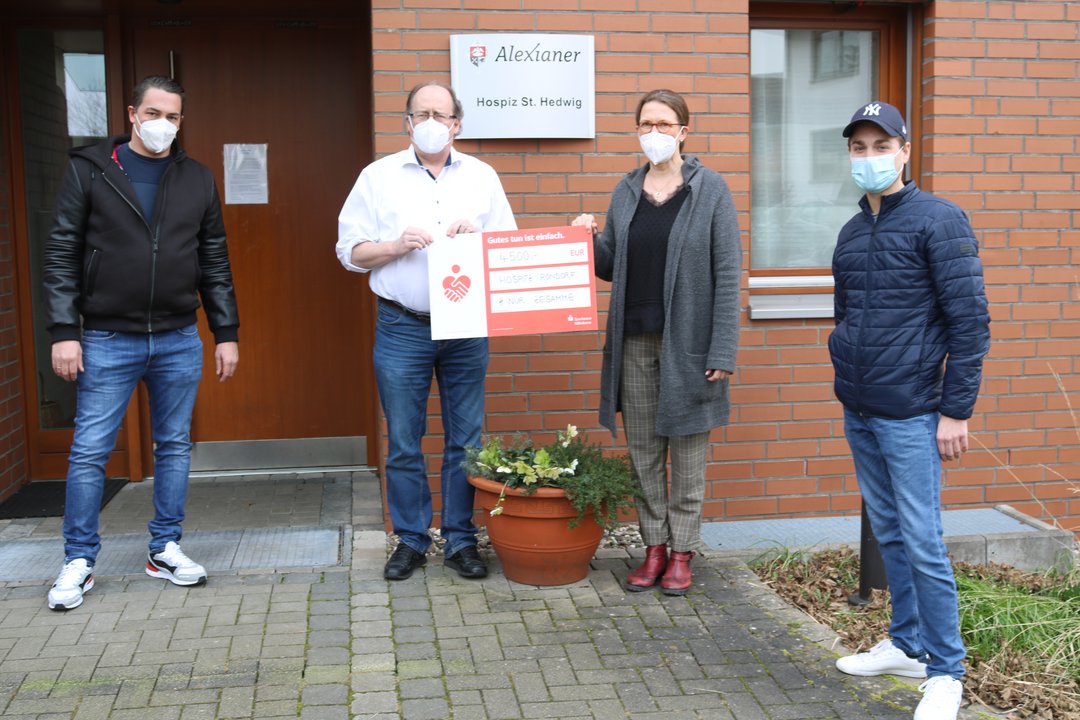 Vier Menschen stehen vor einem Haus, zwei halten einen Scheck in der Hand.